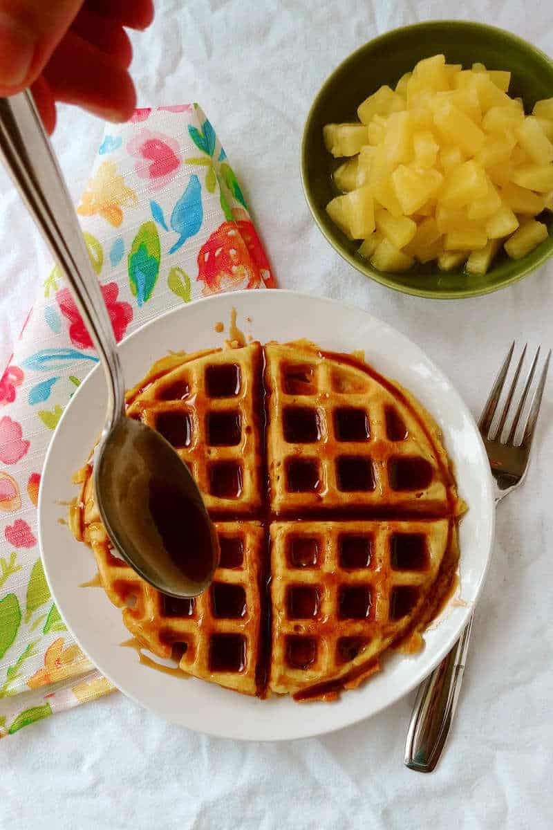 pina colada waffles, with rum sauce being poured on it, with pineapple on the side