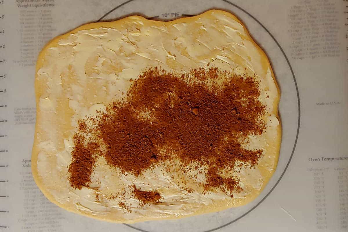 dough for cinnamon rolls, rolled out, with butter spread on it and some cinnamon sugar sprinkled on it