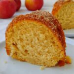 a slice of apple cider donut cake, with another slice and apples in the background