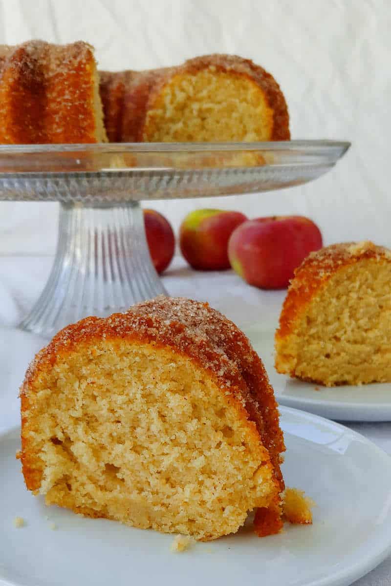slices of apple cider donut cake, with the cake and apples in the background