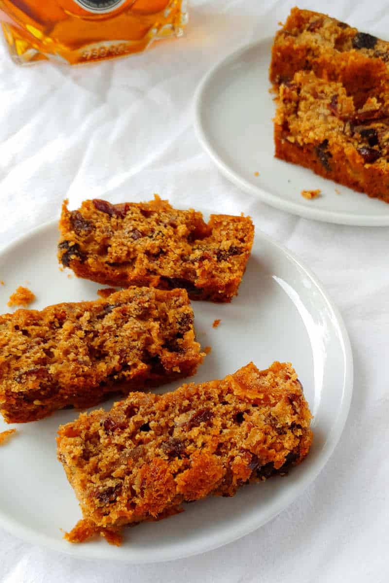 slices of Alton Brown's fruitcake, on plates, with a bottle of brandy in the background