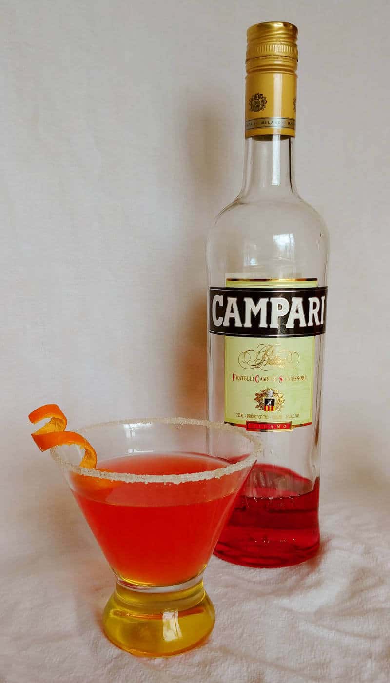 campari margarita, with a sugar-rimmed glass and an orange curl, next to a bottle of Campari liqueur
