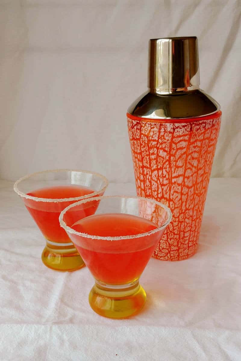 two campari margaritas, in sugar-rimmed glasses, next to a cocktail shaker