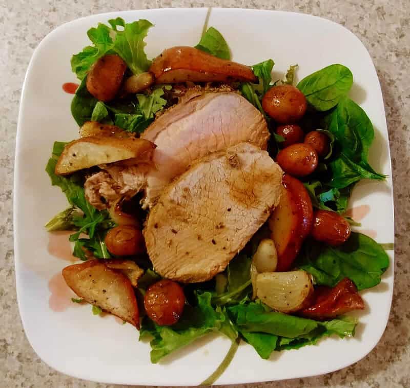 roasted fennel-crusted pork with potatoes and pears, over salad on a plate