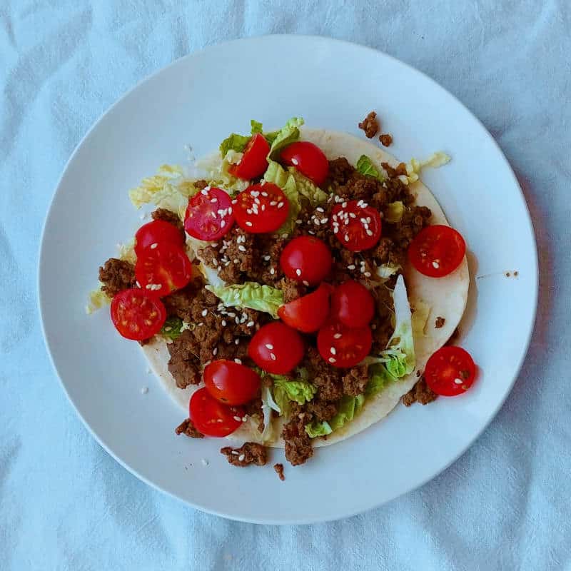 bulgogi tacos with lettuce, tomatoes, and sesame seeds, on a plate