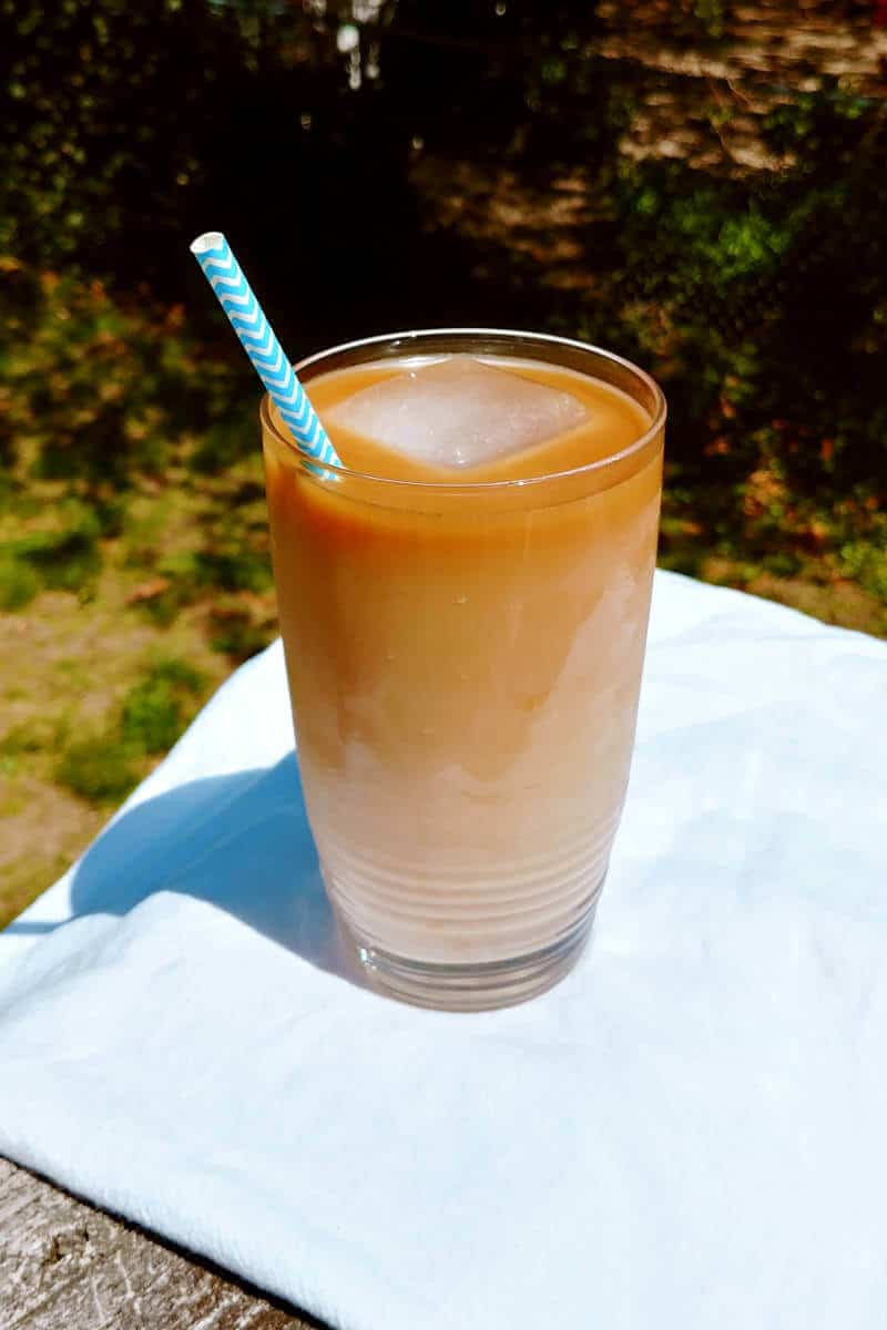 cold-brew iced coffee concentrate, mixed with milk and ice, in a glass with a straw, outside