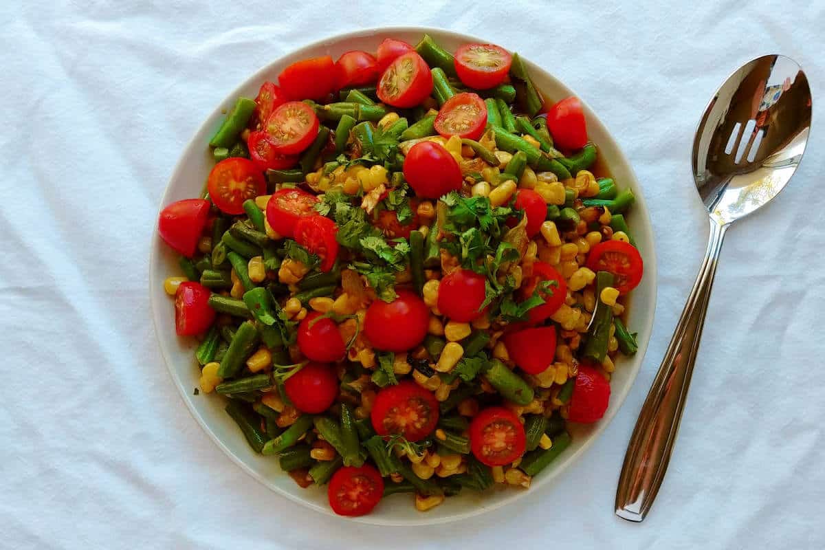 corn and green bean salad with lime dressing, on a plate, with a serving spoon