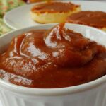 no-sugar-added apple butter, in a white bowl, with english muffins spread with apple butter in the background