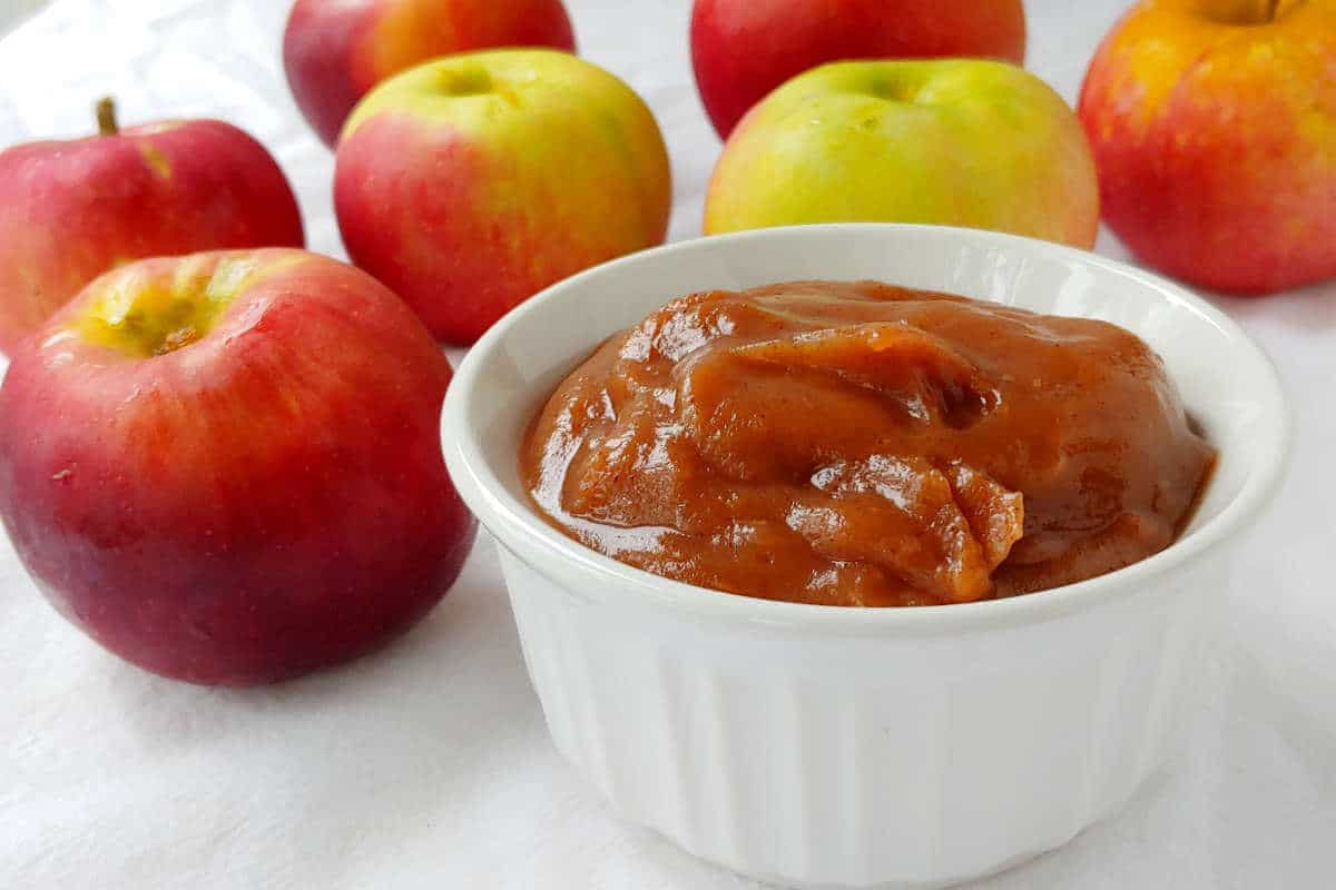 slow cooker apple butter with no sugar added, in a bowl in front of a lot of apples