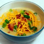 baked potato and bacon soup, in a bowl, topped with bacon, green onions, and cheese