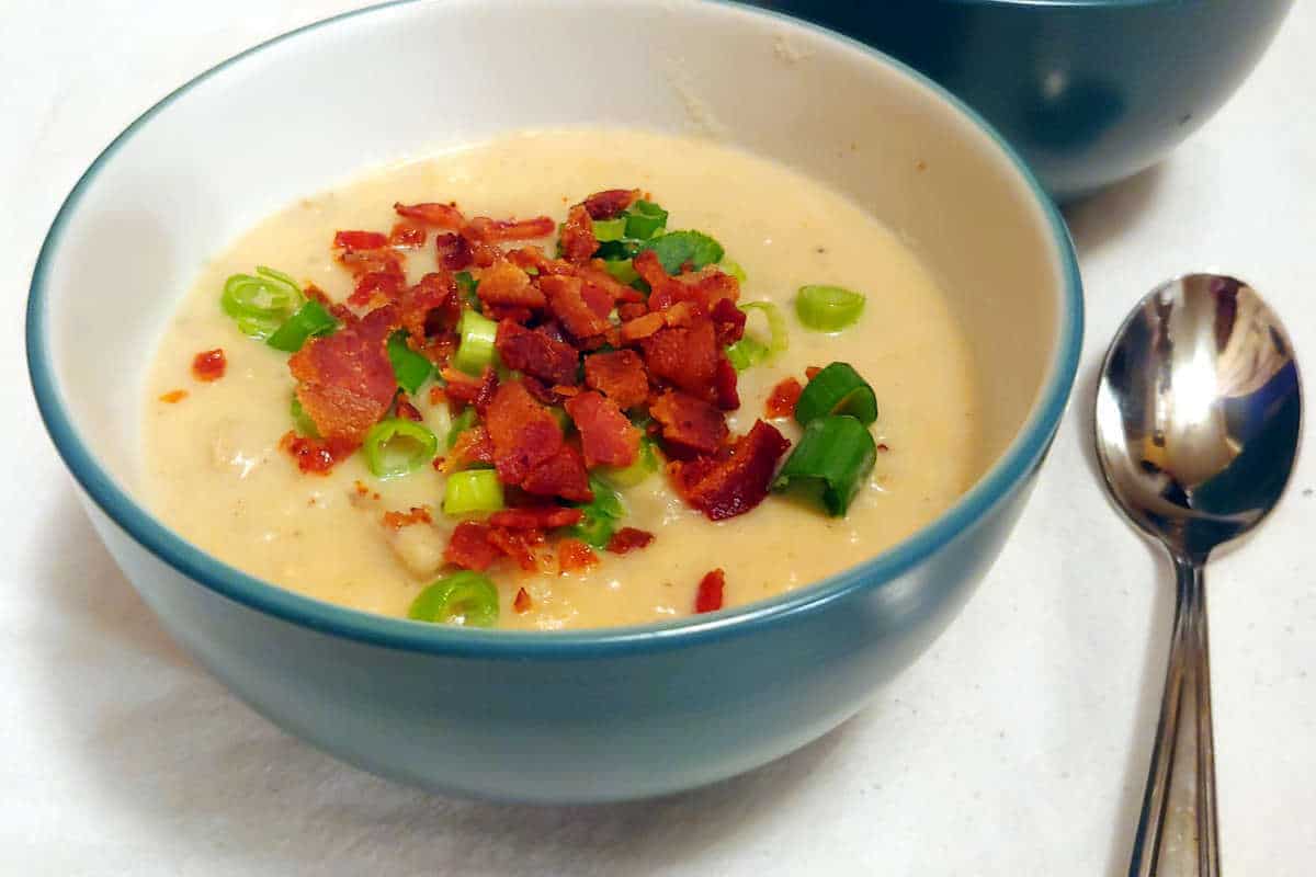 baked potato and bacon soup, topped with green onions and bacon, in a bowl with a spoon