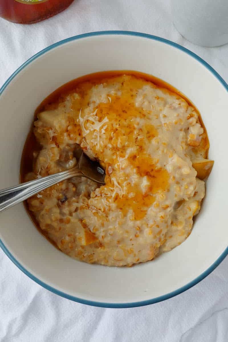 steel-cut oats with walnuts and pear, in a bowl with honey drizzled over it, with a spoon