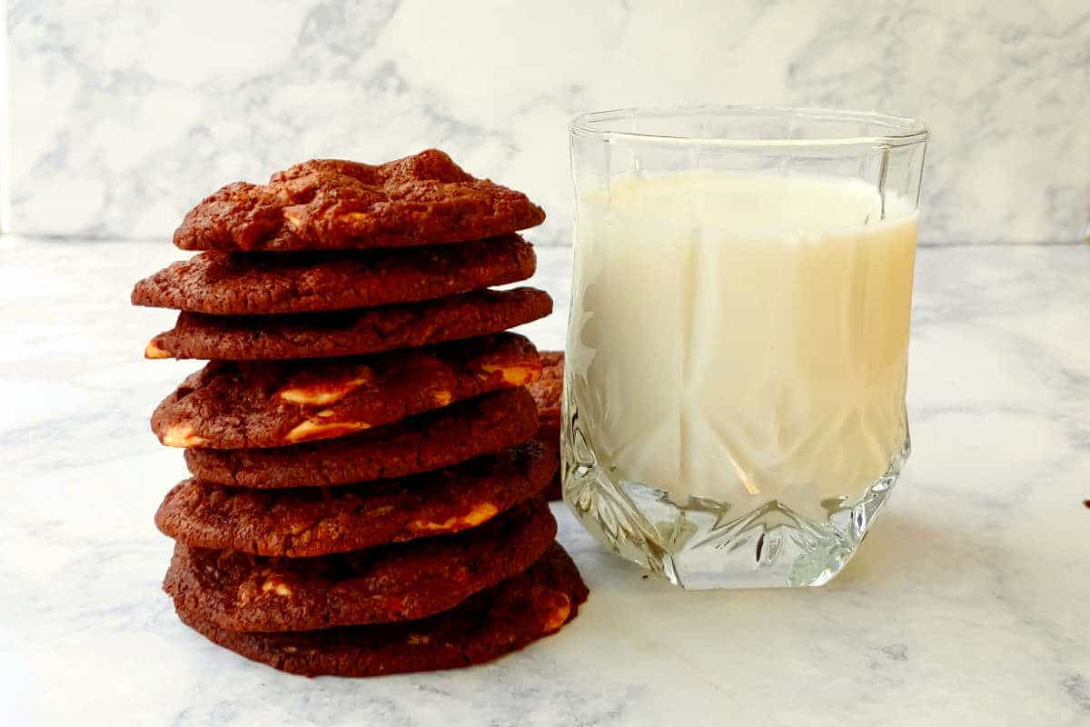 a stack of double chocolate caramel chip cookies next to a glass of milk