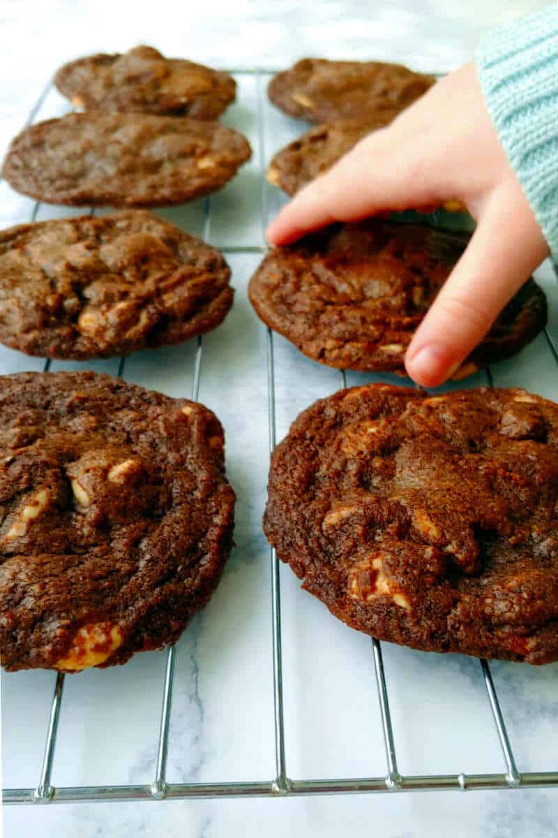 a hand reaching for a double chocolate caramel chip cookie on a cooling rack