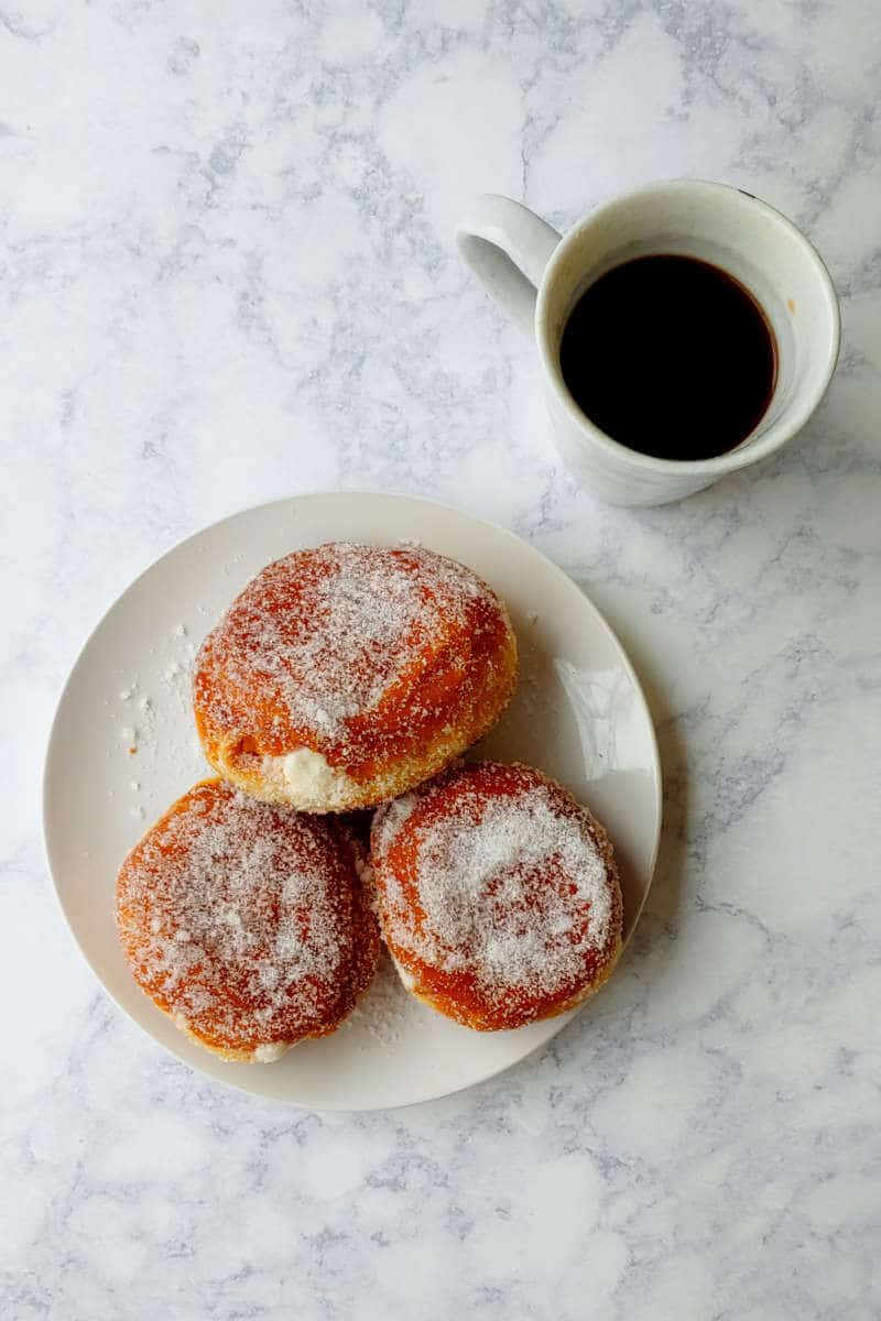 a plate of paczki, with coffee on the side, seen overhead