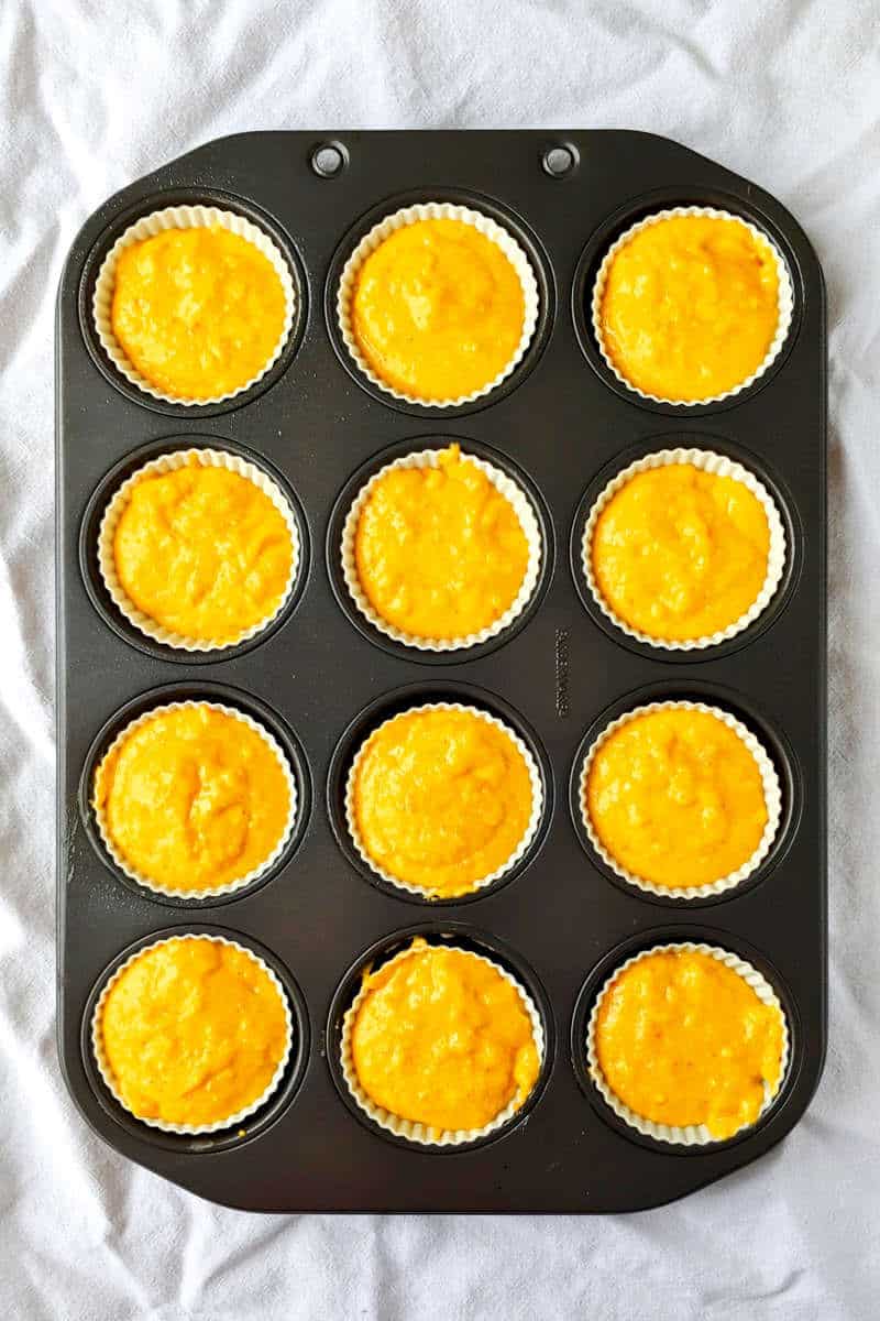 batter for orange cupcakes, in muffin liners in a muffin tin
