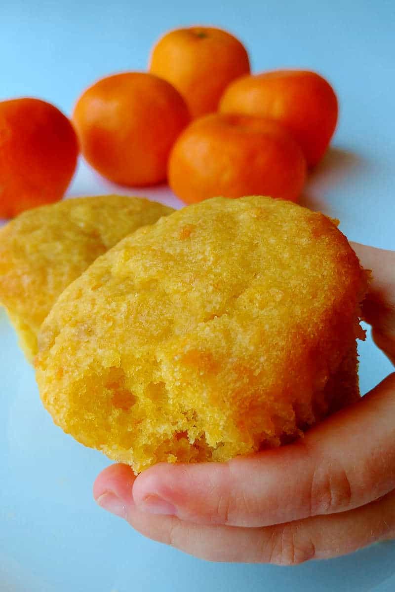 a hand holding out an orange cupcake with a bite taken from it