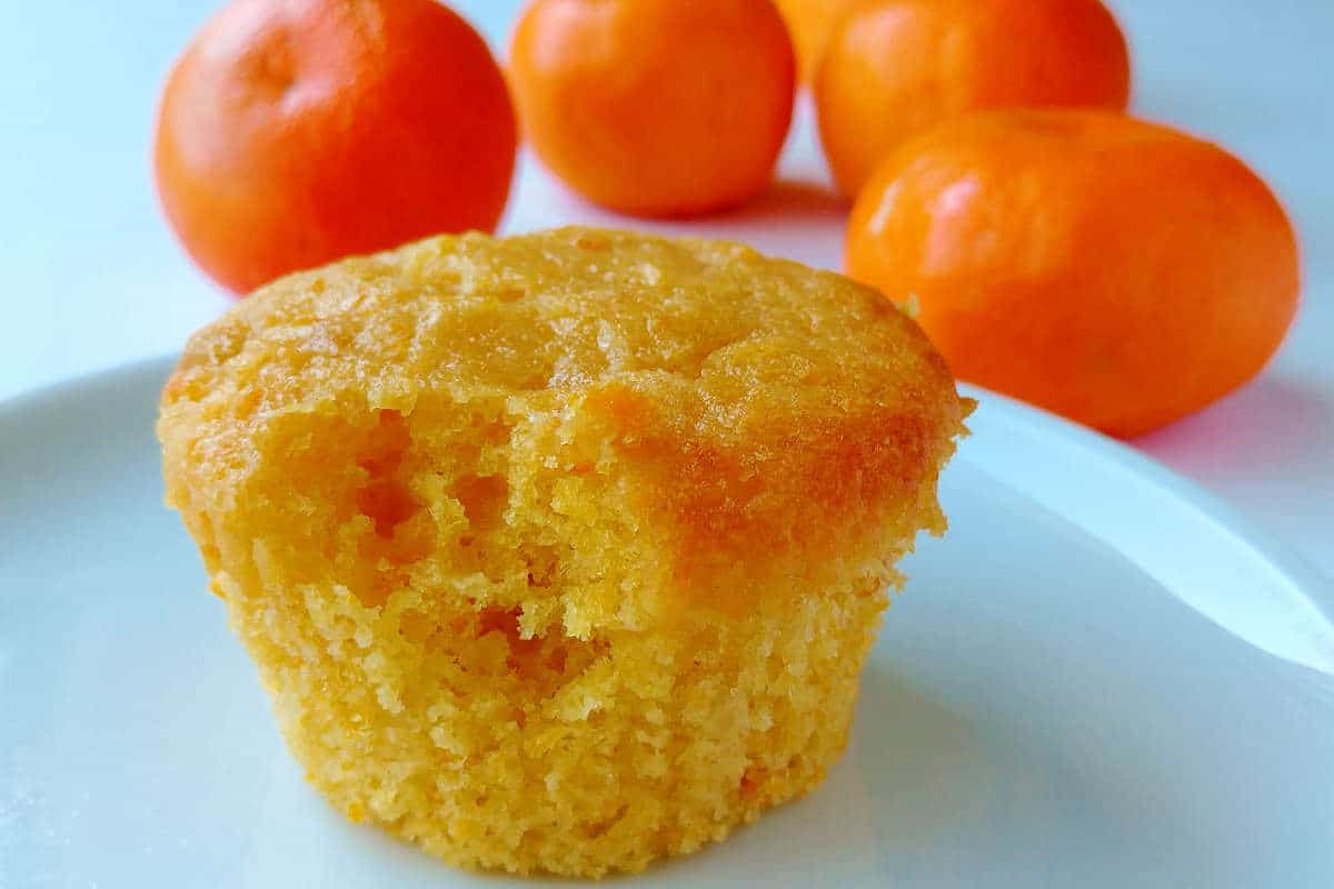 vegan orange cupcake, with a bite taken out of it, in front of clementines