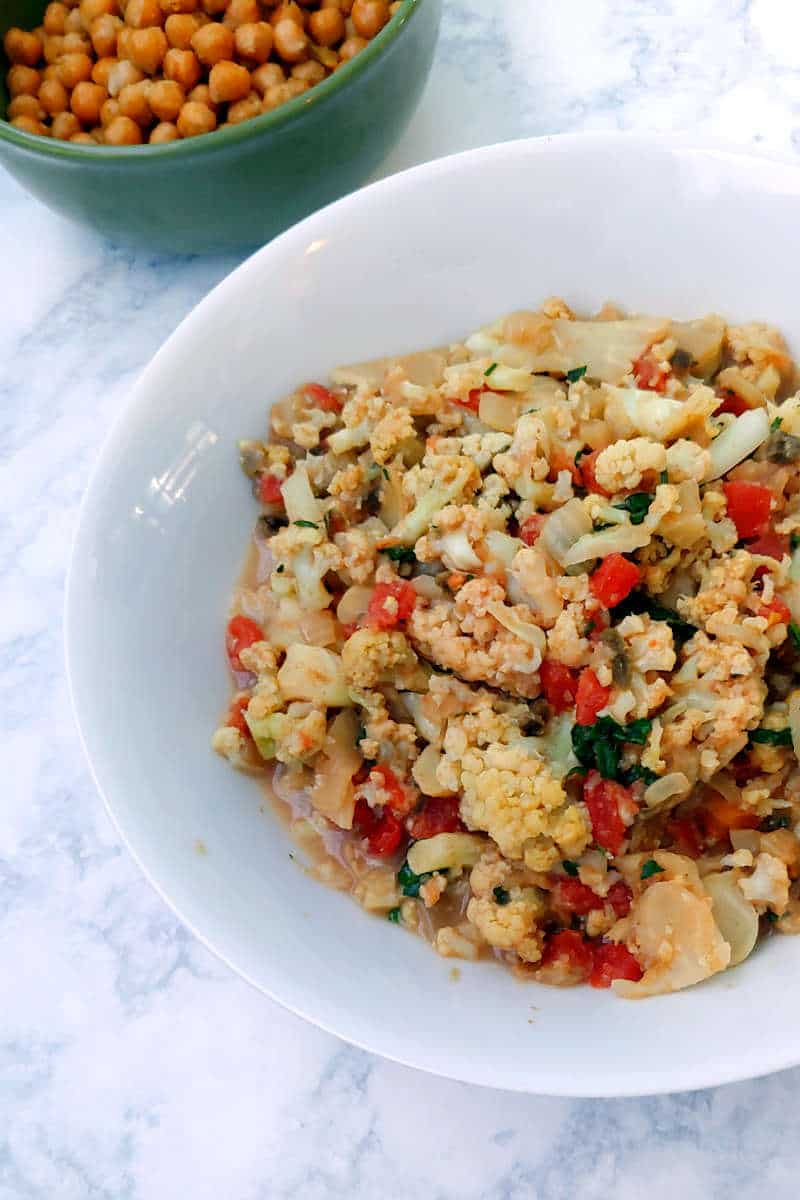 cauliflower curry in a white bowl, with roasted chickpeas in a green bowl