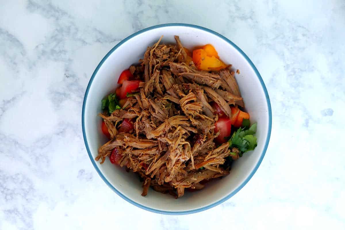 a bowl of barbacoa over beans and bell peppers