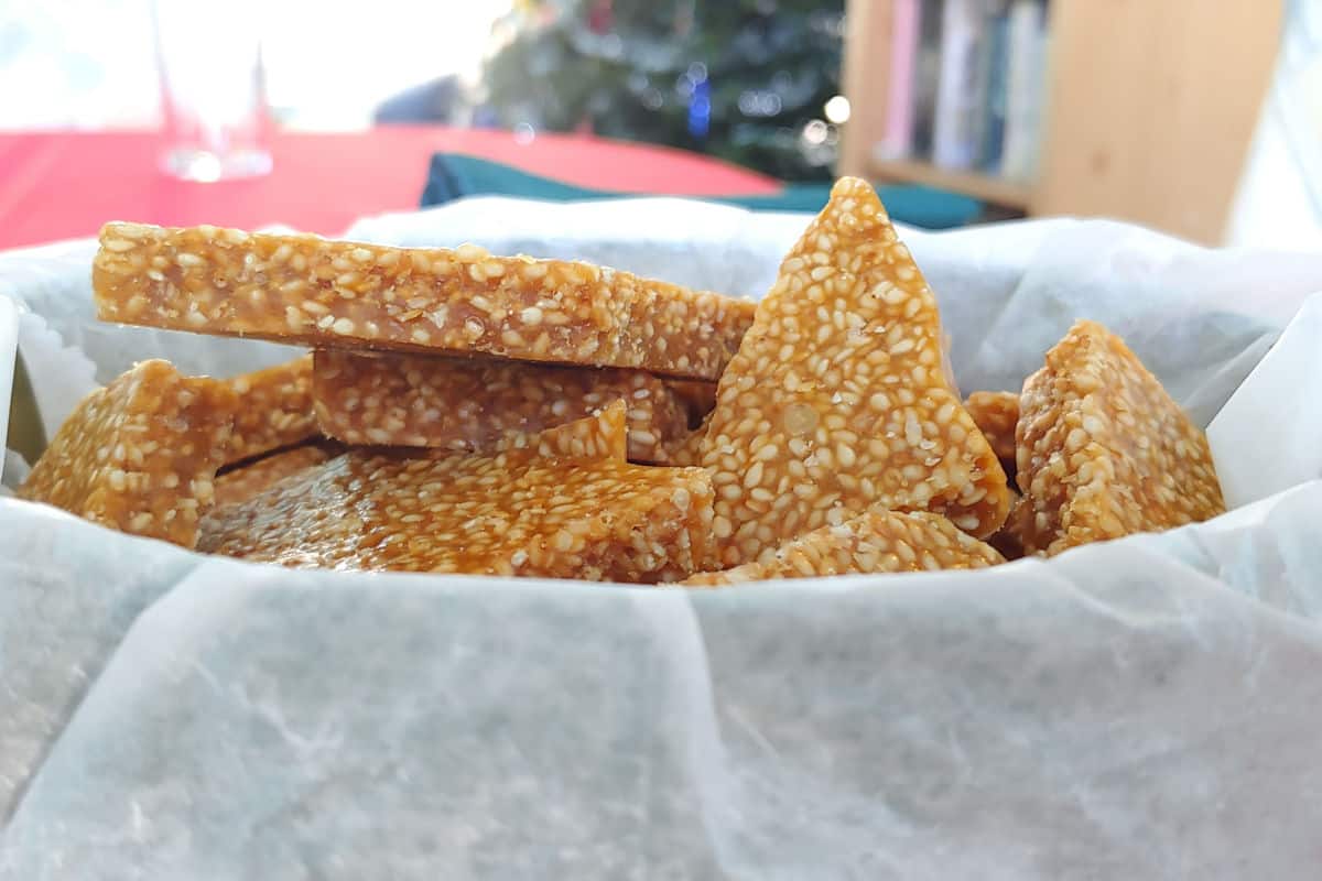 sesame brittle in a tin, with Christmas tree behind it