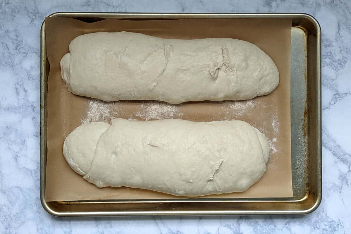 loaves of italian bread dough, shaped and risen, ready to go into the oven