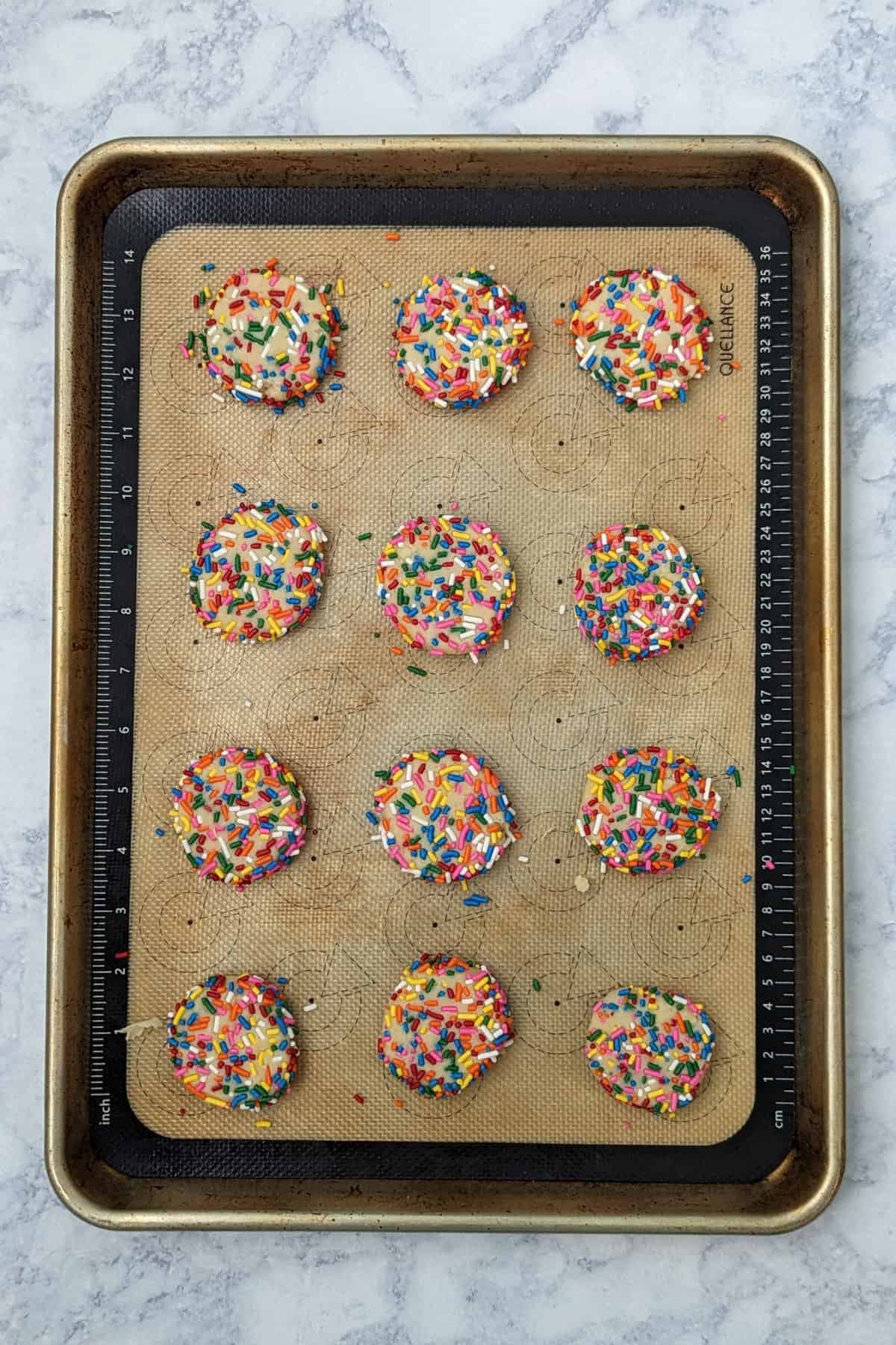 balls of sprinkle cookie dough, flattened out on a baking sheet, before baking