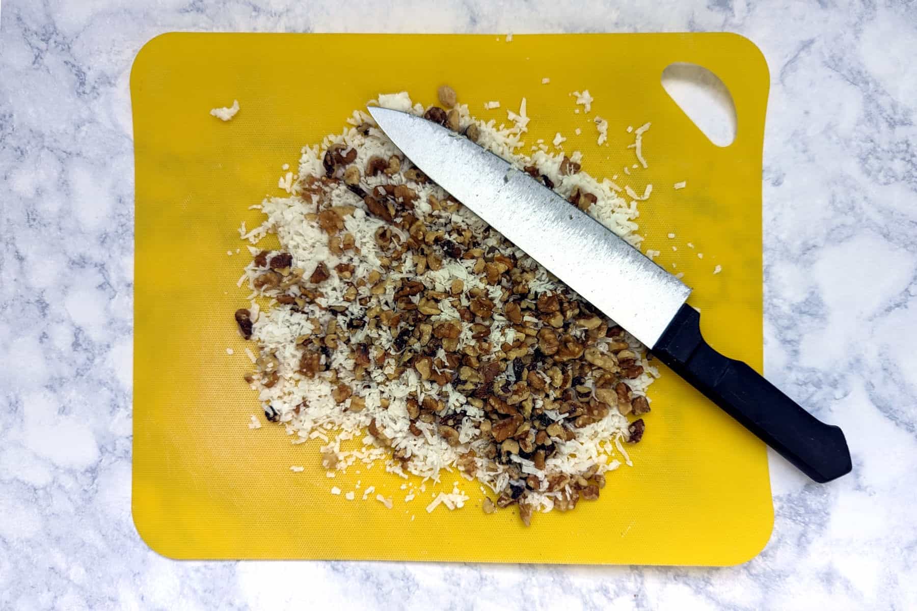 chopped walnuts and coconut on a cutting mat with knife
