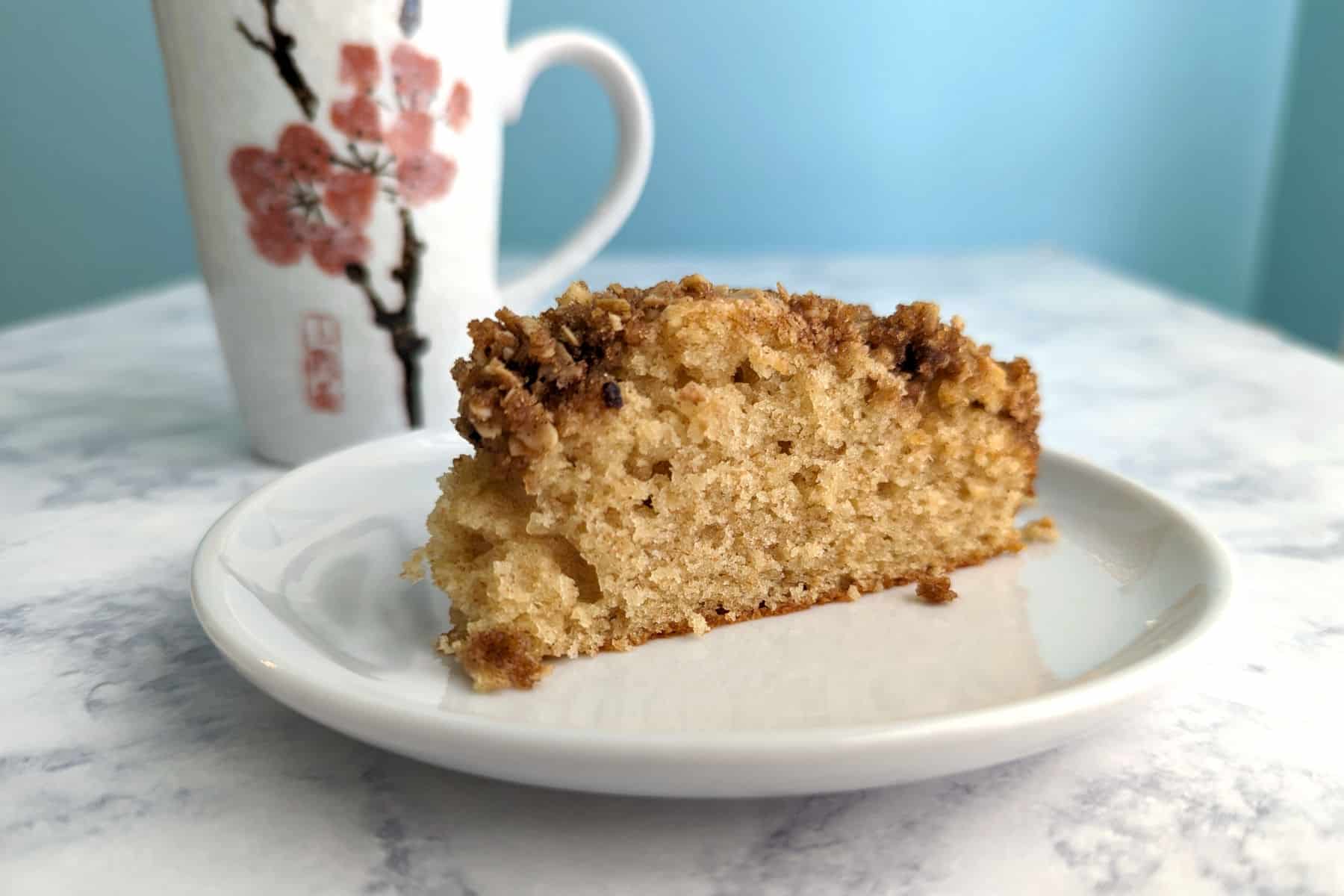 slice of sour cream coffee cake on a plate, with a flowered mug next to it