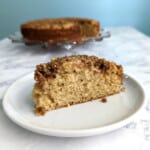 slice of sour cream coffee cake on a plate, with the full cake in the background