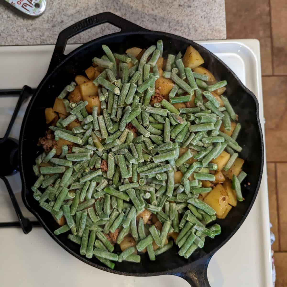 frozen green beans layered on potatoes in a cast iron skillet