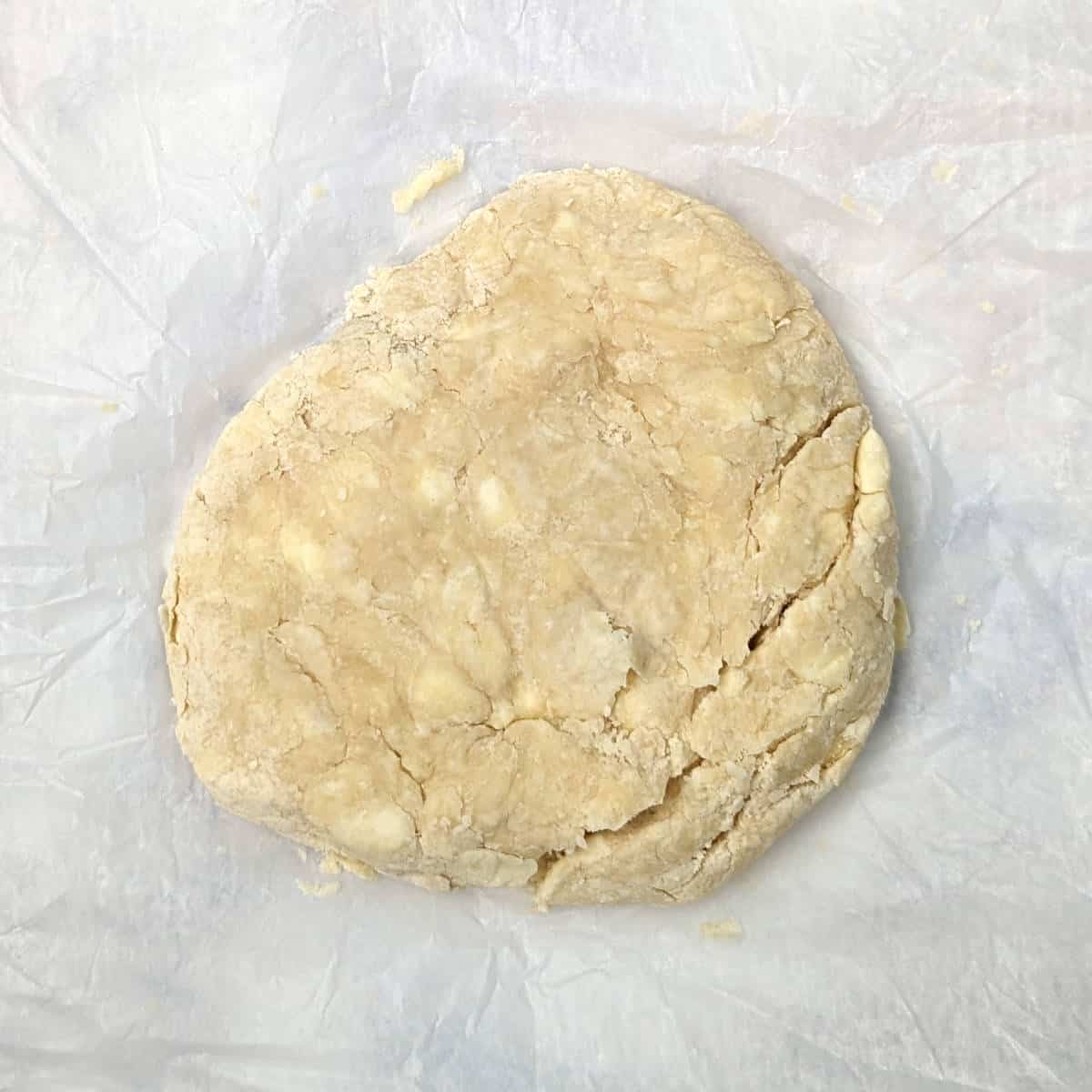 a rough disc of pie crust dough, with large lumps of butter visible. The disc of dough is cracked