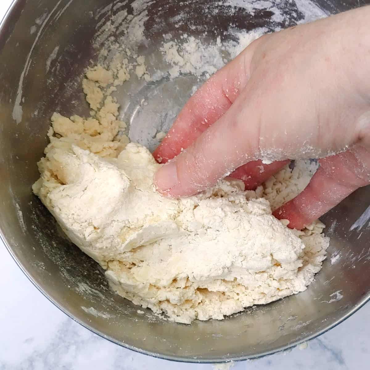 gently molding pie crust dough crumbs together by hand