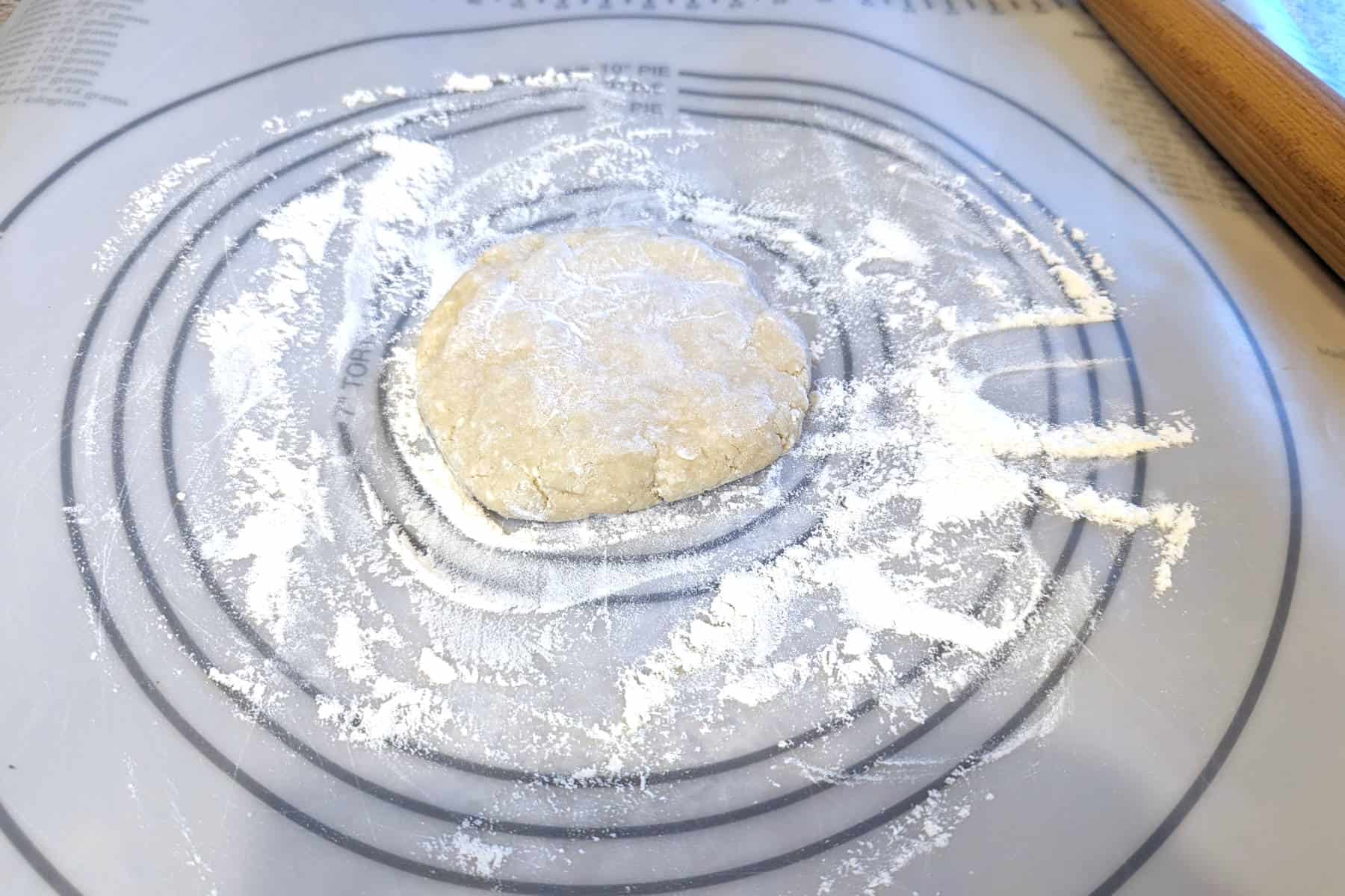 disc of pie crust dough, coated with flour, on a rolling mat