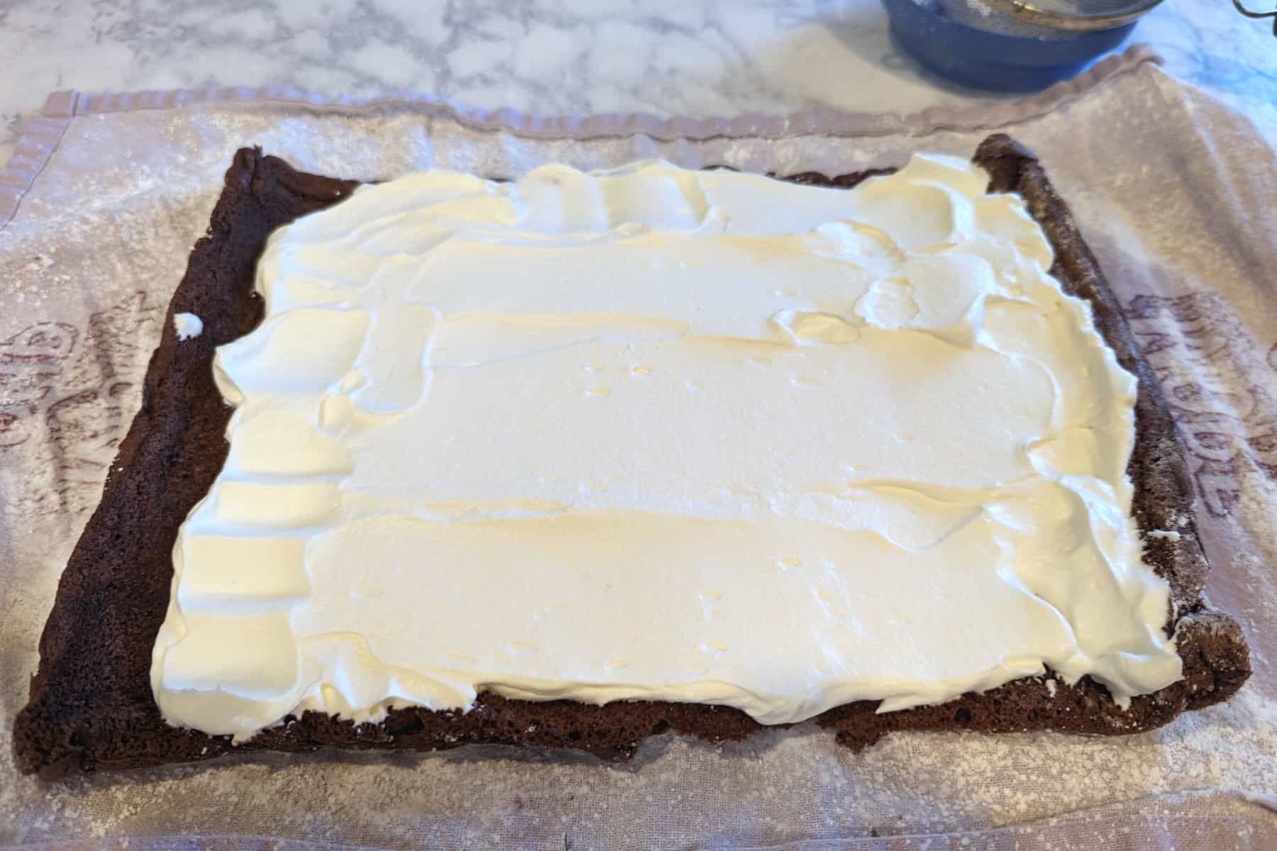whipped cream spread on a chocolate cake, leaving a ½ inch gaps along the side, and 1 inch gap at the end