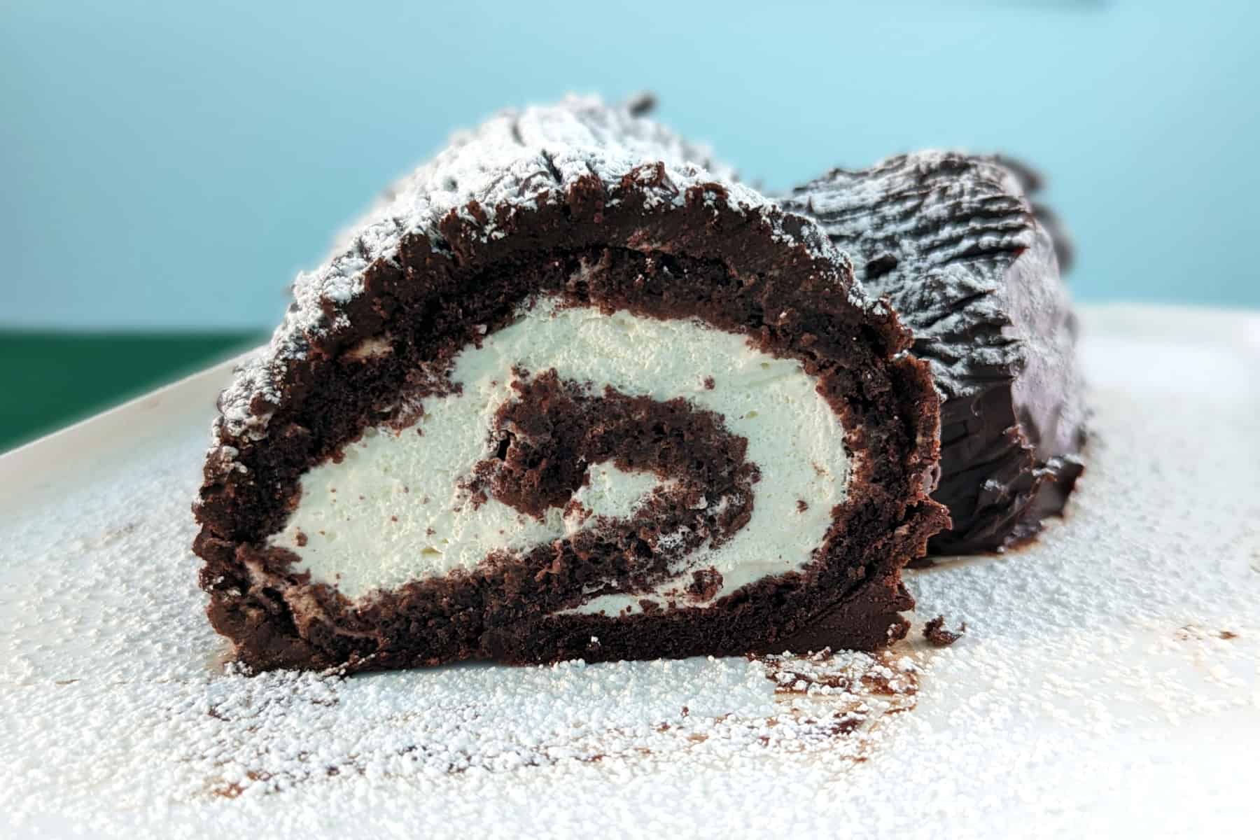 chocolate yule log with a slice missing so you can see the swirl, with powdered sugar snow on top