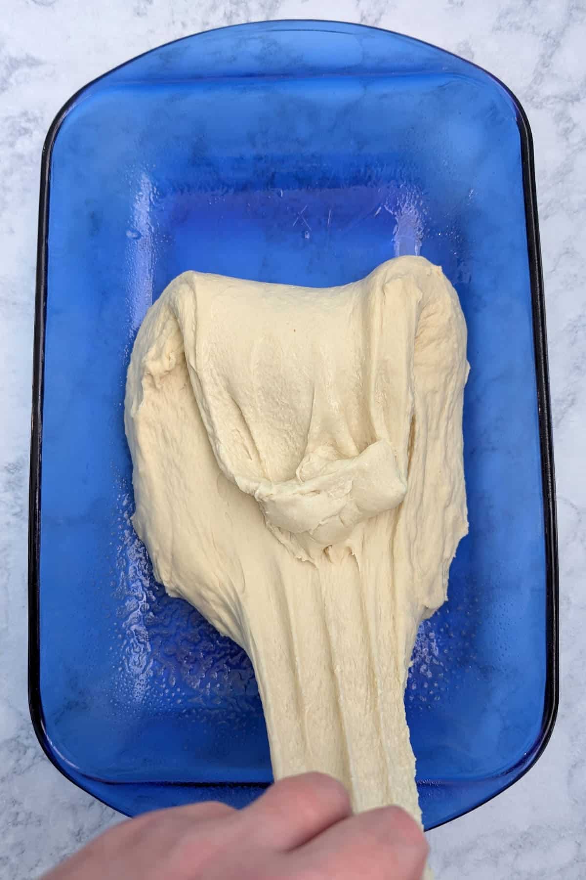 Dough for focaccia in a blue glass baking dish, as I stretch the dough out as part of the kneading process.