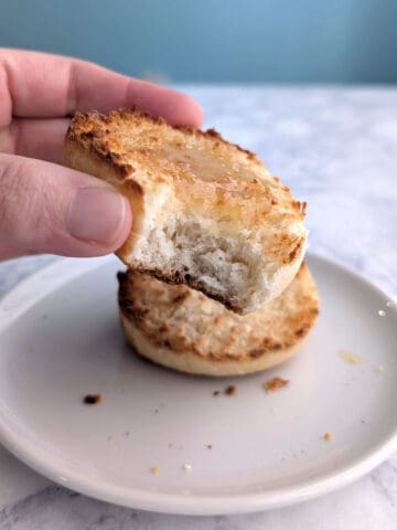 A hand holds half of an English muffin covered with honey, with a bite taken out of it.