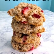 4 strawberry and cream scones, stacked on top of each other, on a table. Text overlay says "Strawberry and Cream Scones. Diced strawberries; vanilla glaze baked on top!"