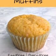 A vegan orange muffin in a pale paper muffin liner, seen up close. Text layover for Pinterest reads: Vegan Orange Muffins. Egg-Free, Dairy-Free, Made with whole oranges!"