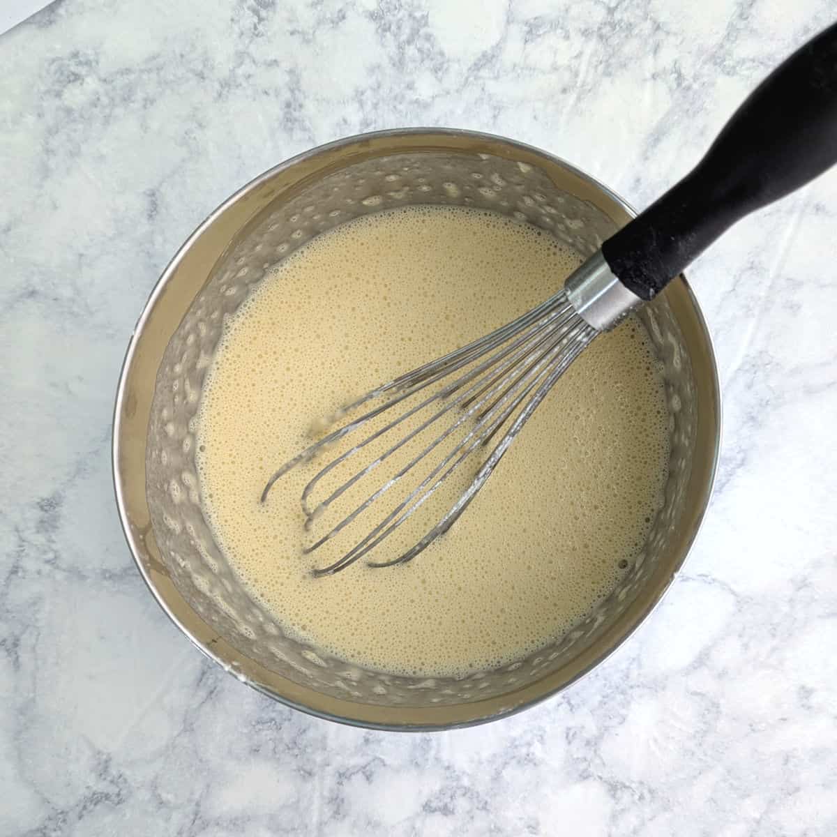 Milk, eggs, flour, and salt whisked together in a bowl, with a wire whisk resting in it.