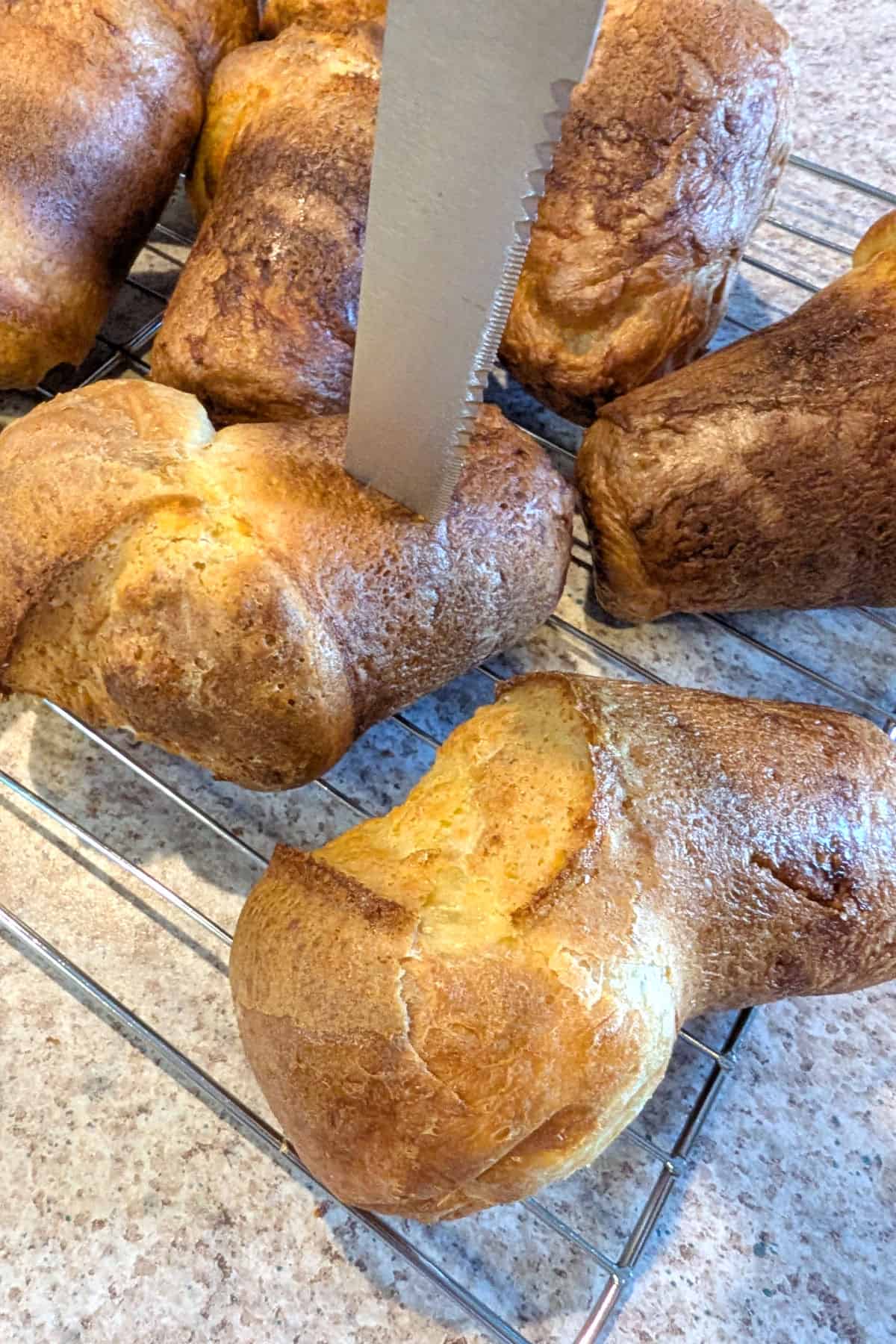 A knife inserted into a popover on a wire rack.