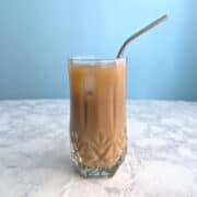 Iced coffee from cold brew coffee concentrate, in a glass with an ice cube and a straw.