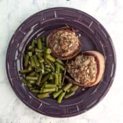 Two Fake Steak patties, wrapped in bacon, alongside green beans, on a purple plate. Text overlay for Pinterest reads "Fake Steak. AKA Mock Filet Mignon. Just 6 Ingredients!"
