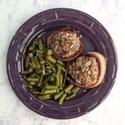 Two Fake Steak patties, wrapped in bacon, alongside green beans, on a purple plate. Text overlay for Pinterest reads "Fake Steak. AKA Mock Filet Mignon. Just 6 Ingredients!"