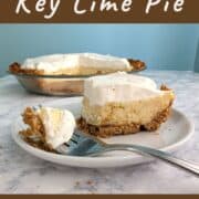 A fork with a bite of key lime pie rests on the plate with the remaining slice. The rest of the pie is in the background. Text overlay for Pinterest reads "Homemade Key Lime Pie. Cool & Creamy. Tart & Delicious!"