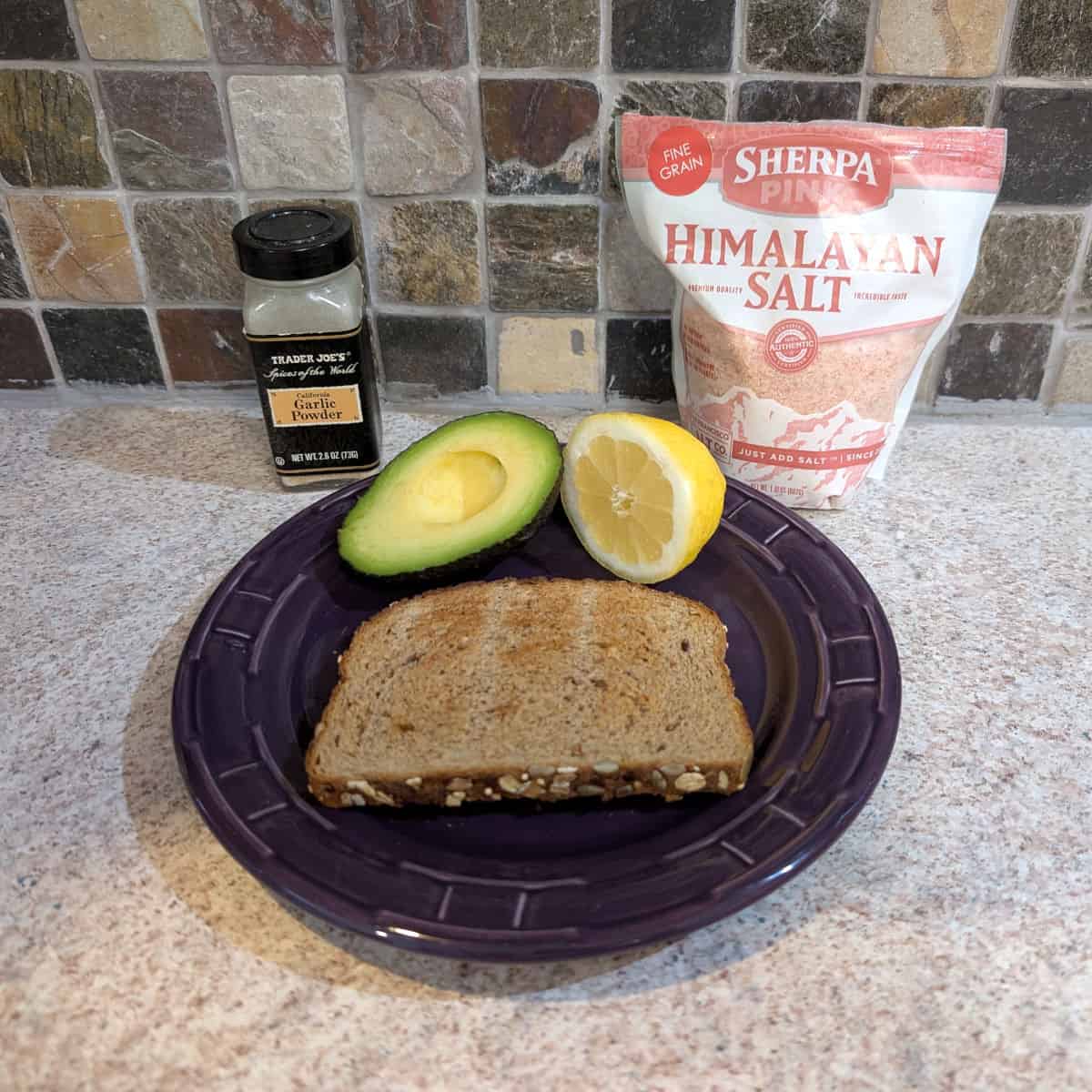 Ingredients for avocado toast: a slice of toasted bread, half an avocado, half a lemon, garlic powder, and salt.