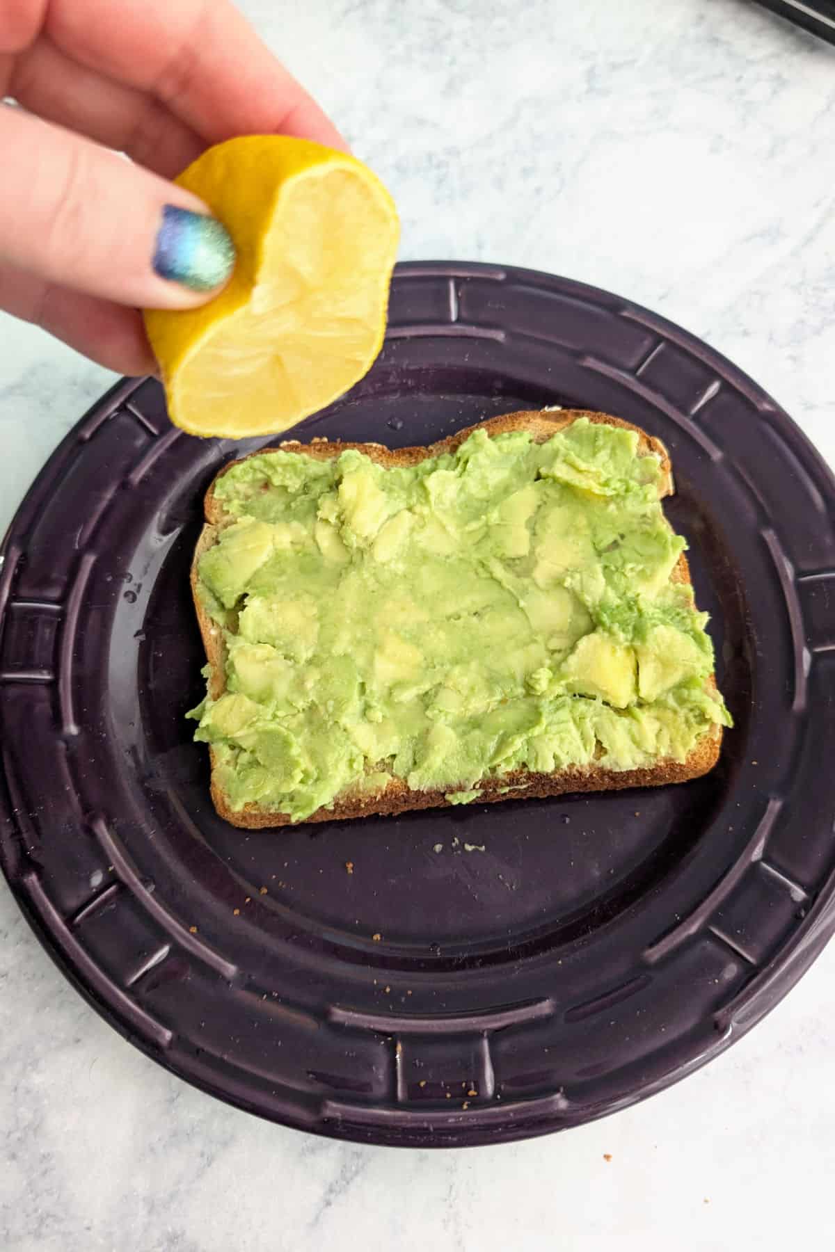 A hand squeezes lemon onto a slice of avocado toast.