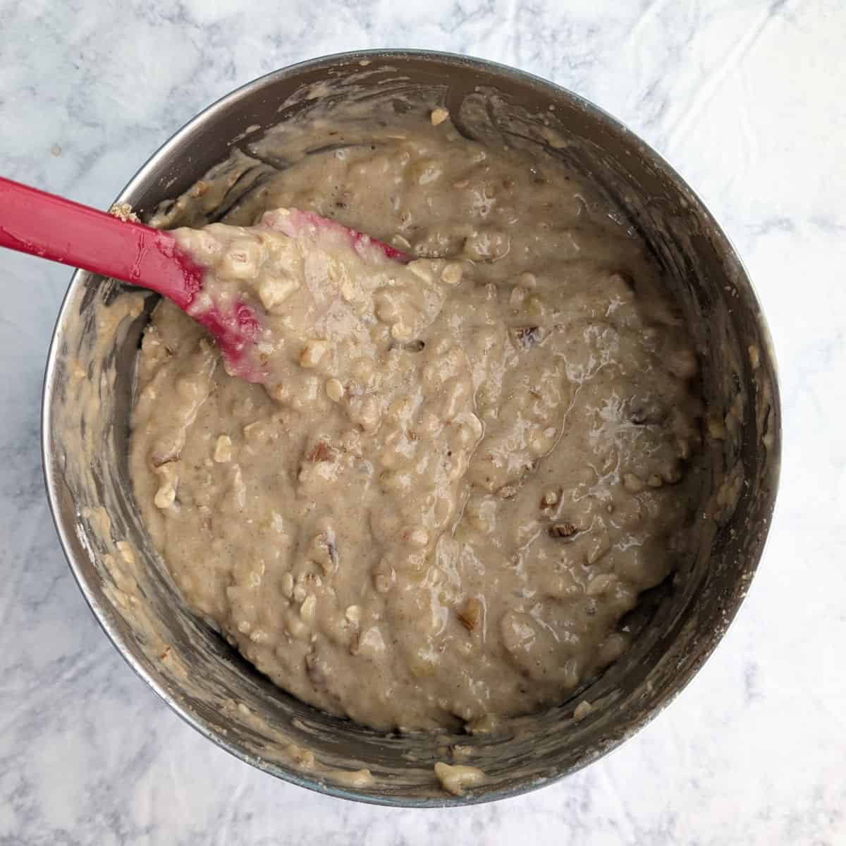Banana bread batter with nuts in a metal bowl.