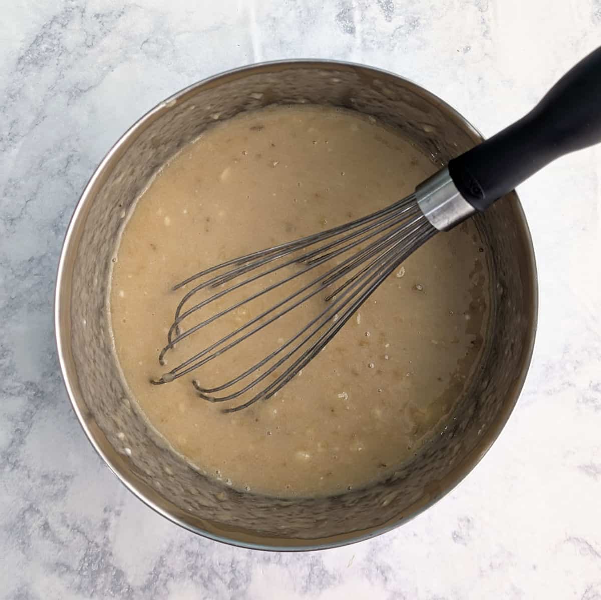 Wet ingredients for banana bread, mixed together in a bowl, with a whisk.